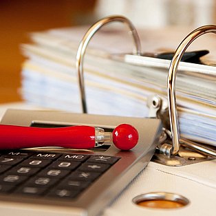 Ein Taschenrechner und eine aufgeschlagener Ordner auf einem Schreibtisch